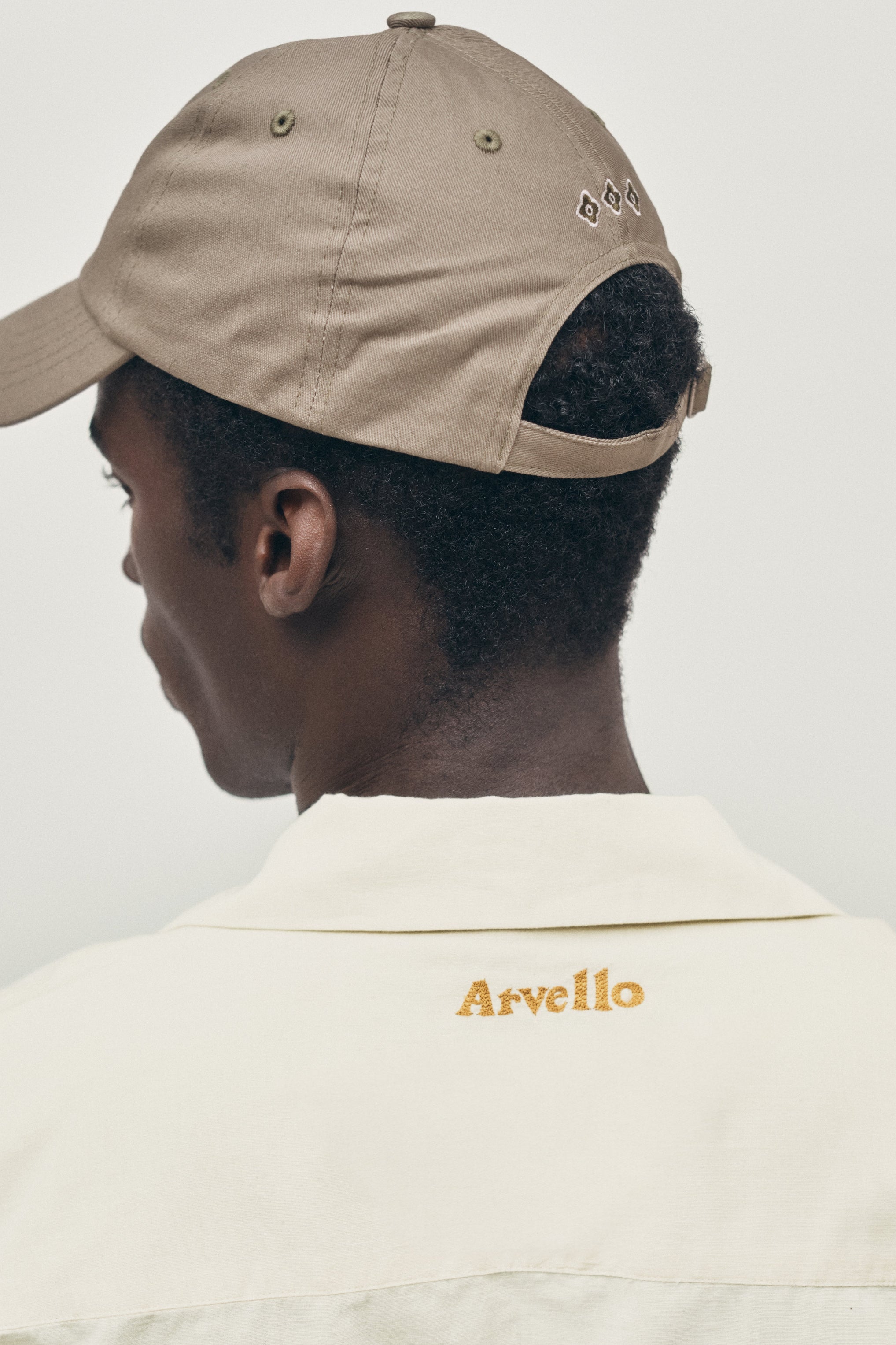 Person wearing a beige cap and shirt with 'Arvello' branding on a plain background