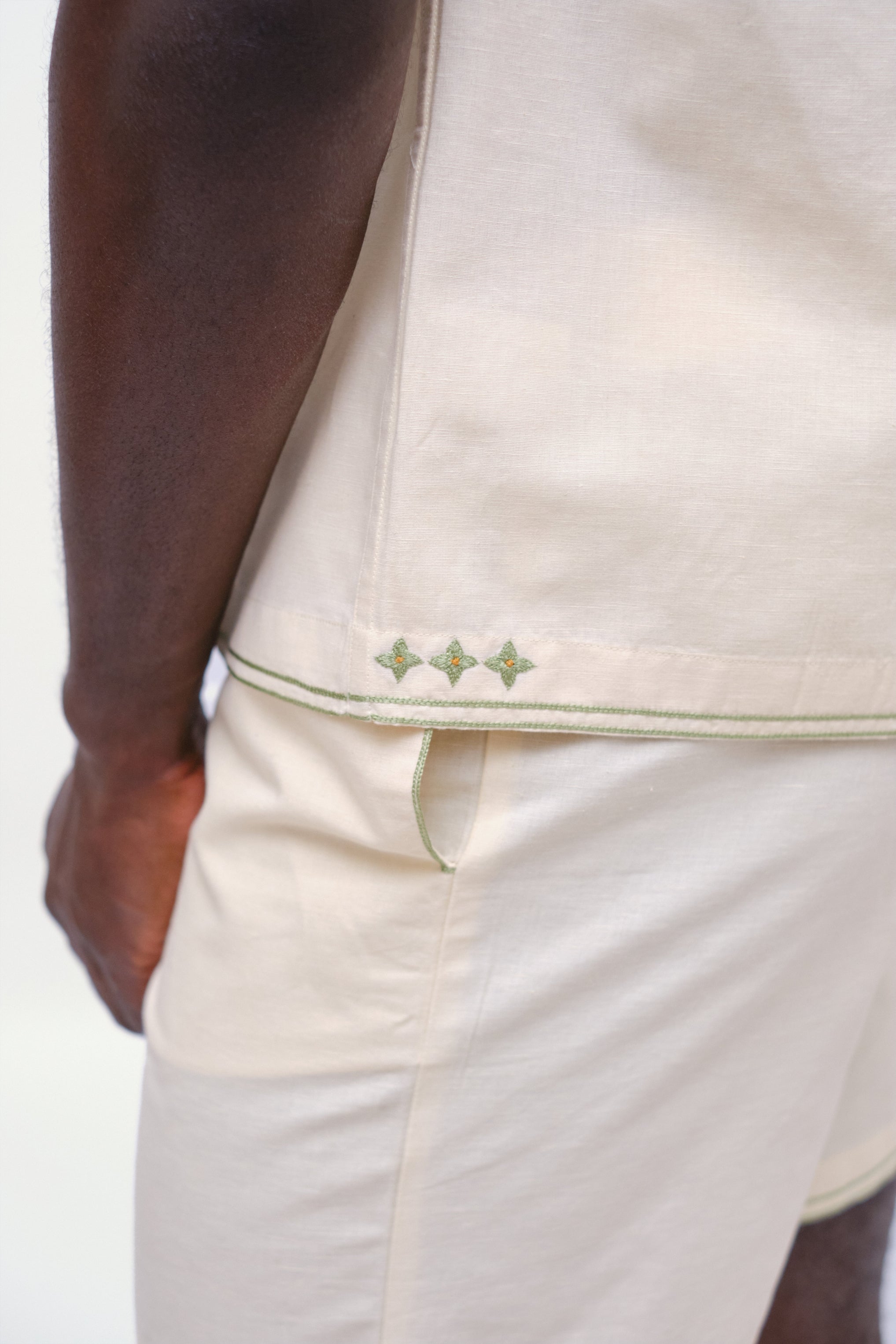Close-up of a person wearing a beige shirt with green stitching detail.