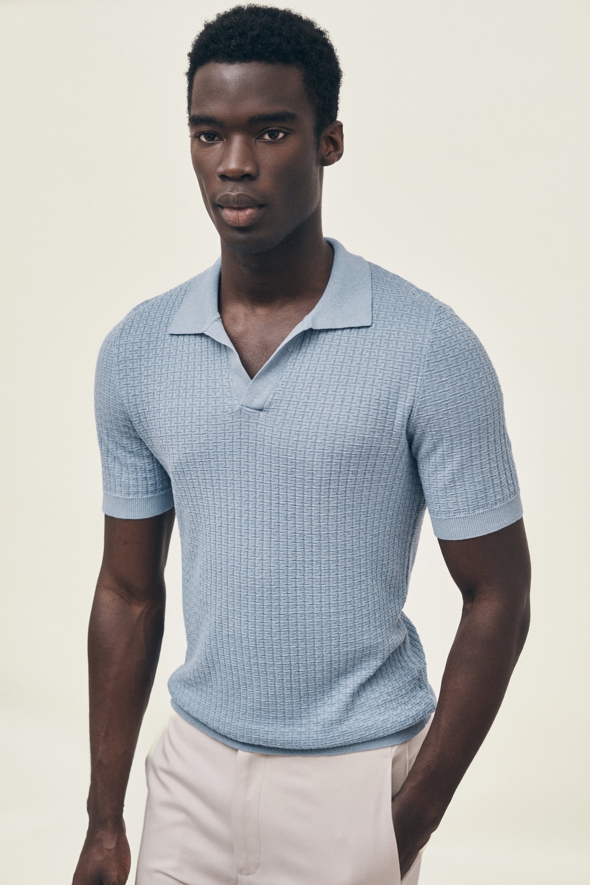 Man wearing a light blue textured polo shirt against a beige background
