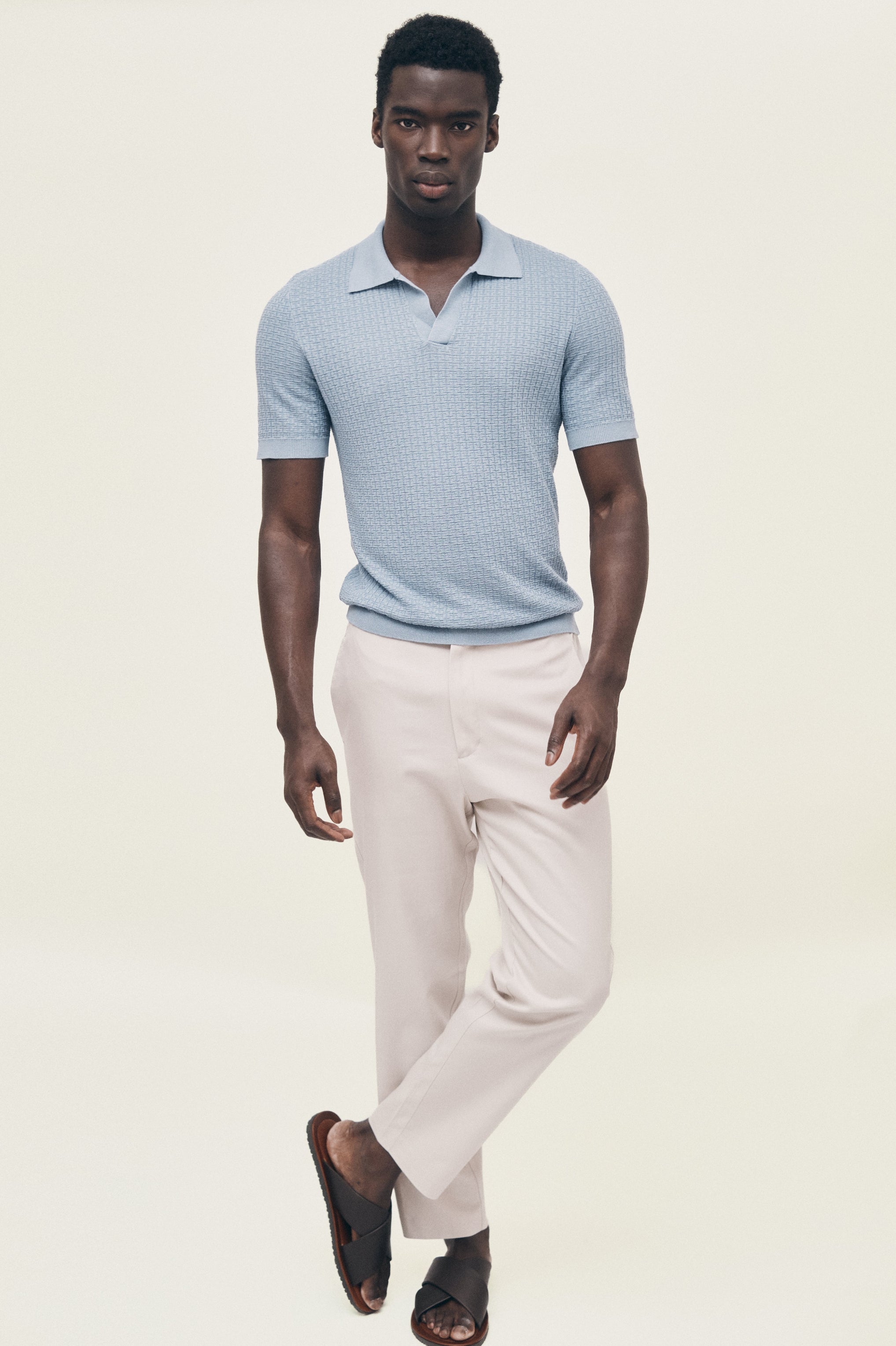 Man wearing a light blue polo shirt and white pants on a plain background