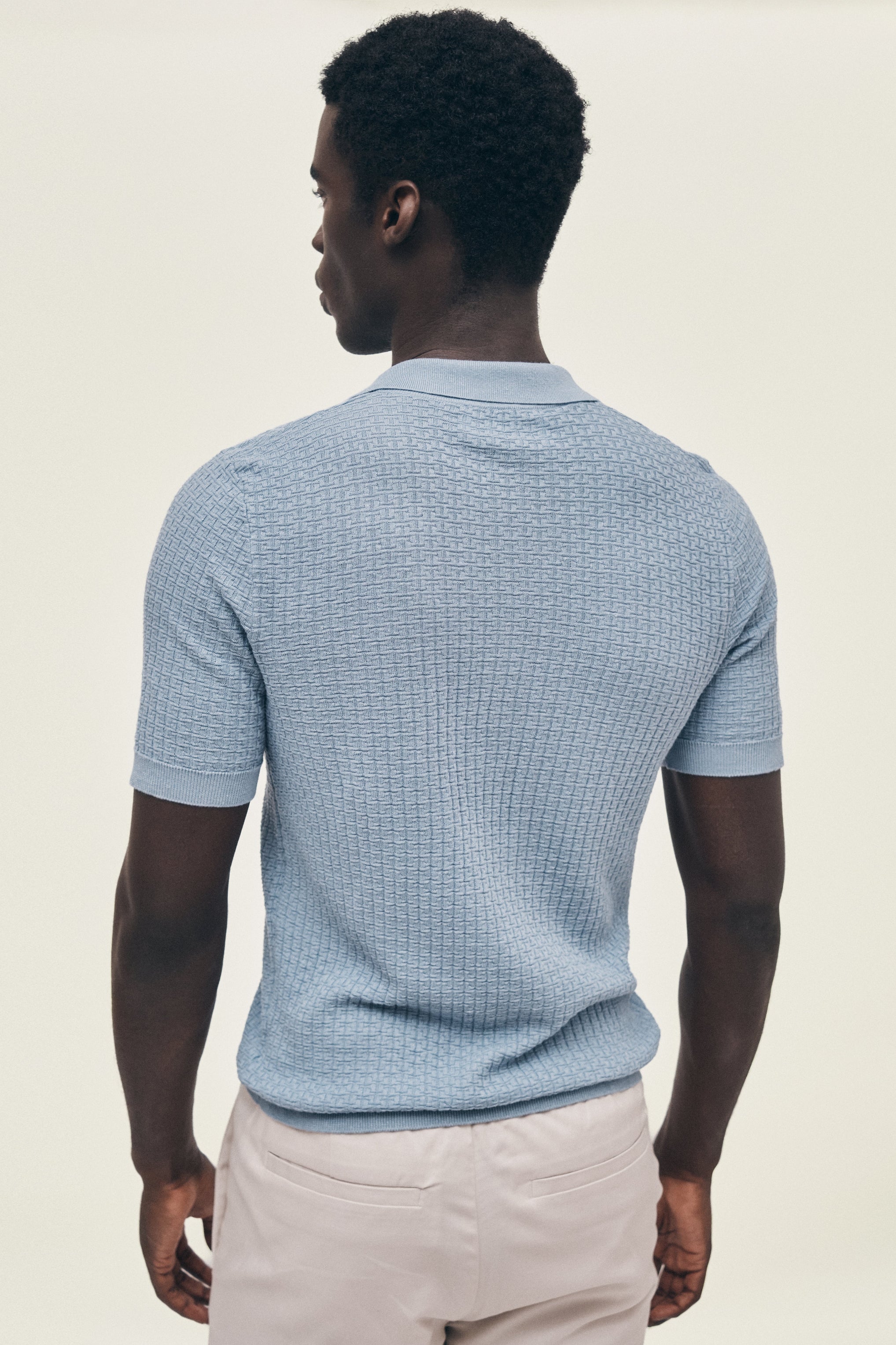 Man wearing a light blue textured polo shirt on a beige background